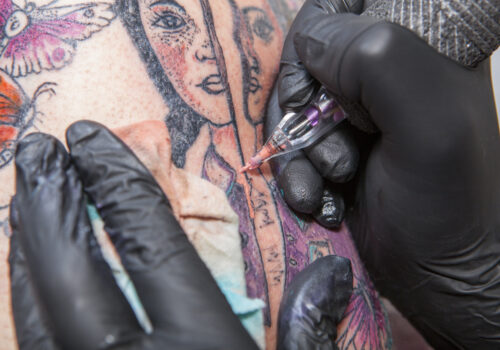 Tattoo artist applies tattoo to arm. She is filling with flesh-coloured ink the tattoo
